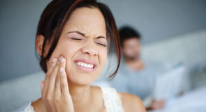 Woman with jaw pain holding jaw.